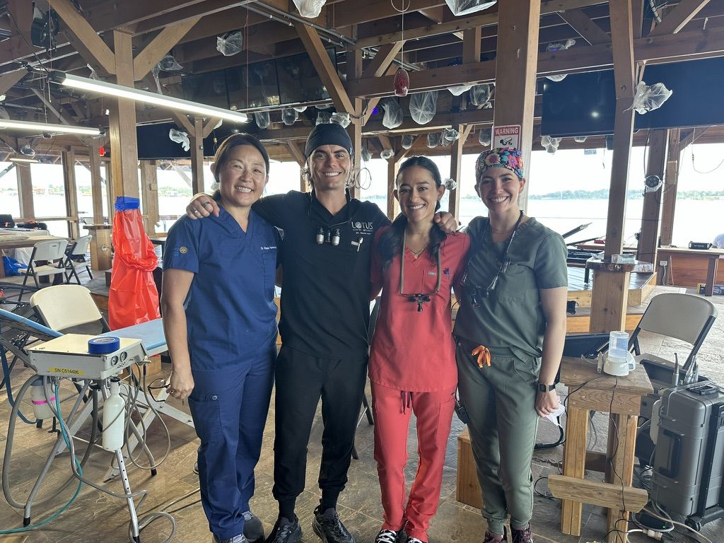 Four volunteers in scrubs at an open air dental clinic by the water
