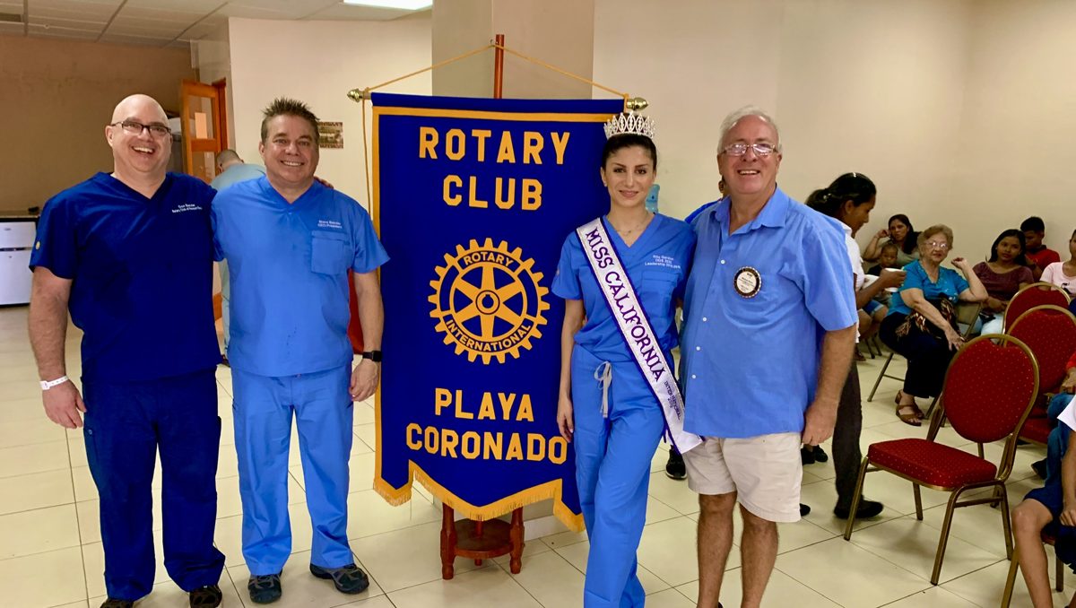 Volunteers in blue scrubs beside the Rotary Club of Playa Coronado banner at a dental clinic
