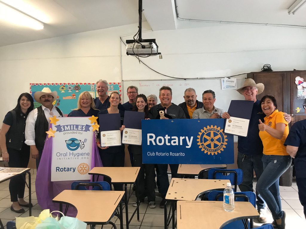 Volunteers and Rotarians hold certificates and a Club Rotario Rosarito sign in a classroom