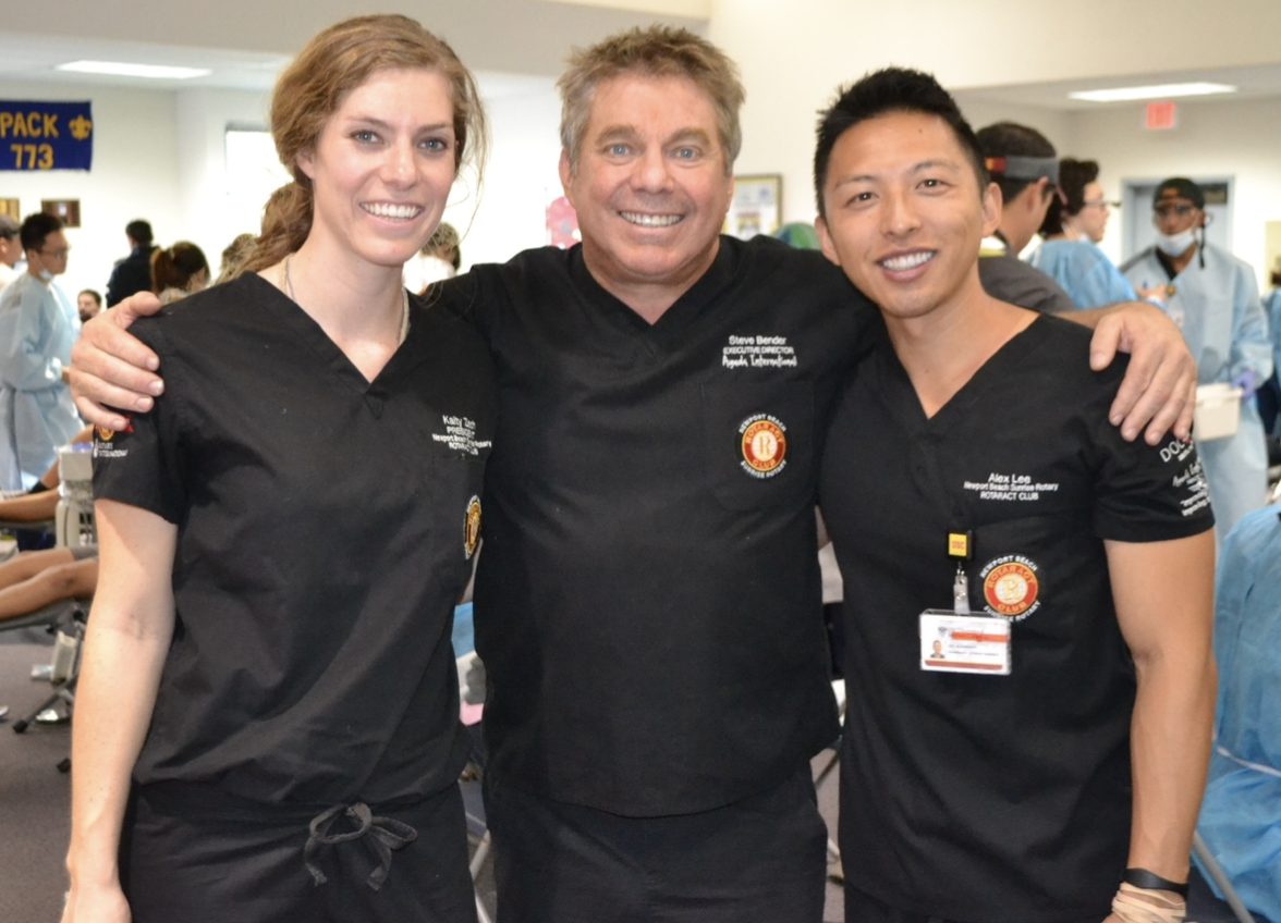 Three volunteers in black Newport Beach Sunrise Rotaract scrubs at a busy dental clinic