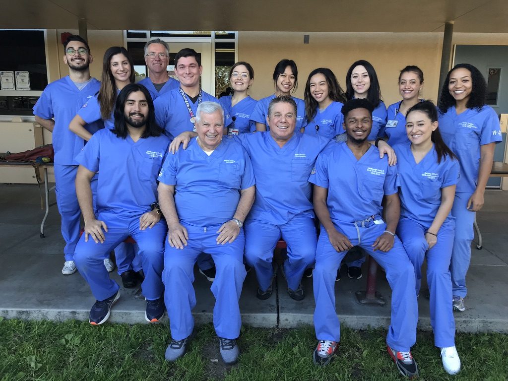 A large volunteer dental team in blue scrubs smiles for a group photo